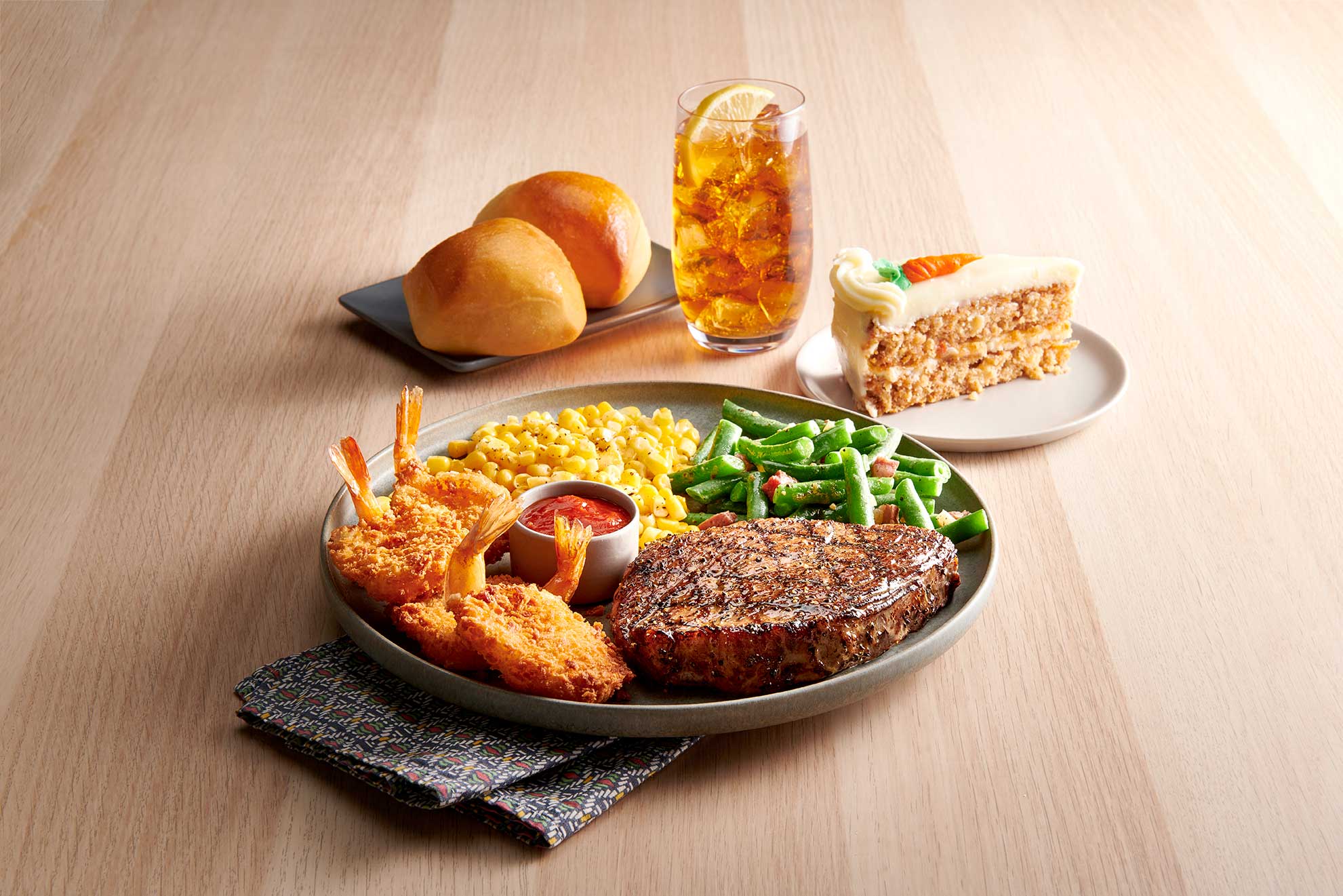 Golden Corral buffet items plated, sirloin steak, butterfly shirmp, grean beans, yeast rolls and carrot cake with iced tea.